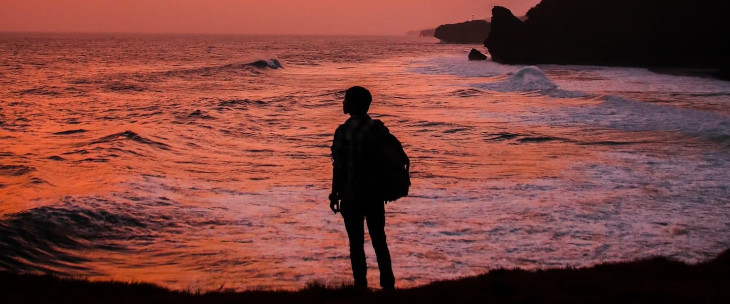 A person standing at the shoreline watching the sunset